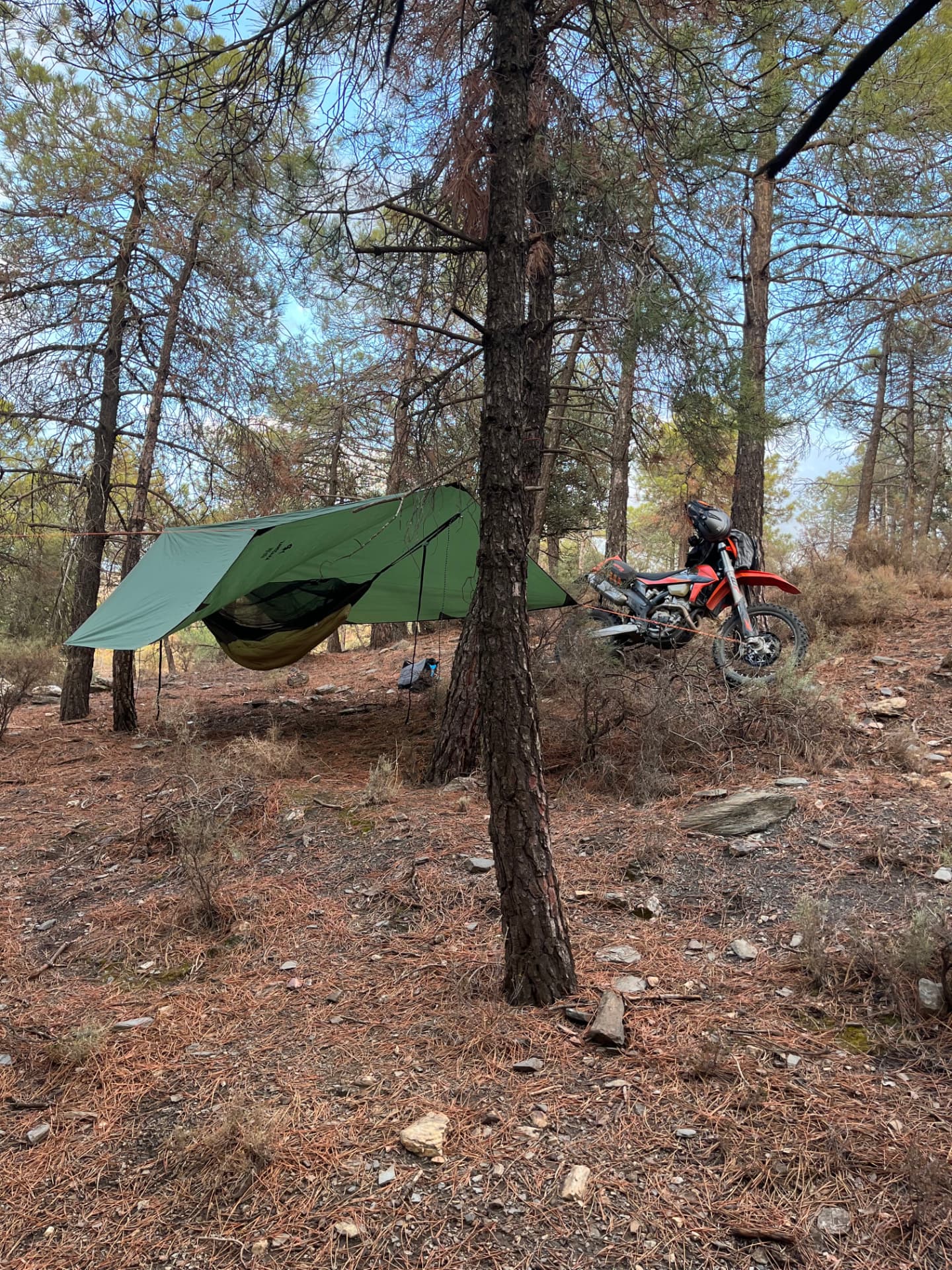 Enduro motorcycle beside a hammock camp in the forest