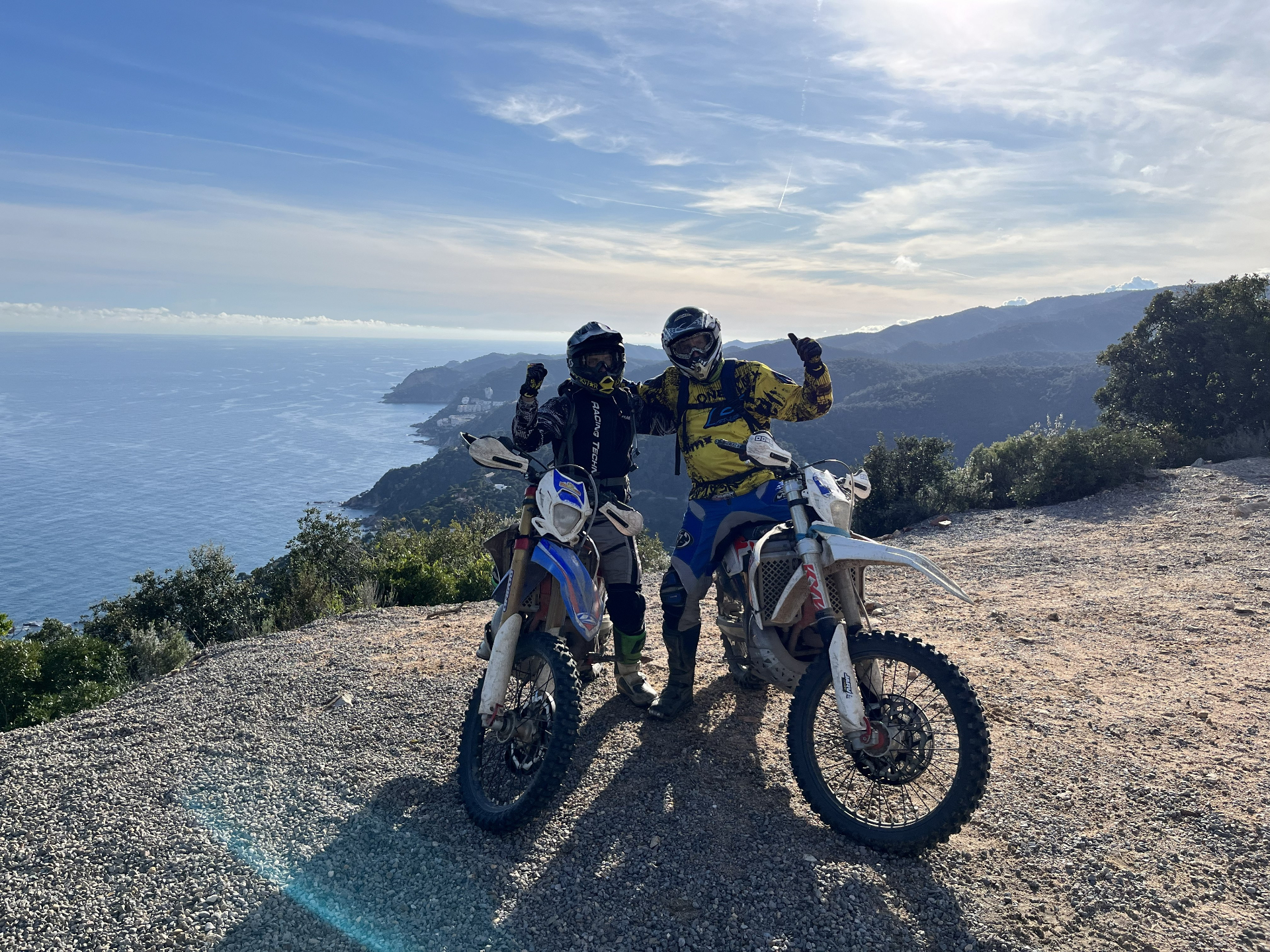 Two enduro riders with motorcycles overlooking the Mediterranean coast near Platja d'Aro